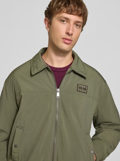 Männermodel trägt olivgrüne Regular Fit Bomberjacke mit abnehmbarem Teddy-Kragen von Tommy Jeans, Struktur glatt, Nahaufnahme Oberkörper. Herren Bomberjacke / Blouson
