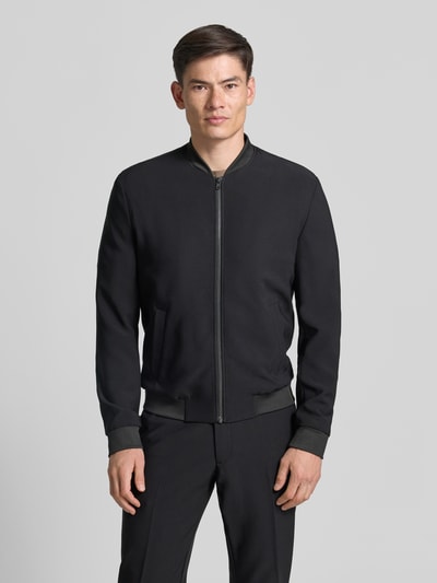 Männermodel trägt Blouson mit seitlichen Eingrifftaschen von MCNEAL in Schwarz, Regular Fit, Stehkragen, elastische Abschlüsse, Ganzkörperansicht von vorne. Material-Mix mit Stretch-Anteil, Reißverschluss, Rückenlänge 65 cm, Schulterbreite 45 cm, Brustweite 60 cm, Ärmellänge 71 cm.