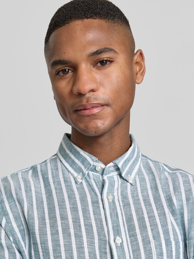 Mężczyznamodel nosi Slim Fit Freizeithemd aus reinen Leinen od Christian Berg Men, kołnierzyk typu button down, krój slim fit, listwa guzikowa, len, długi rękaw, sportowe mankiety, paski, niebiesko-biała kolorystyka, długość tyłu w rozmiarze M: 79 cm, szerokość w rozmiarze M: 48 cm, długość rękawów w rozmiarze M: 65 cm, zbliżenie na górną część ciała
