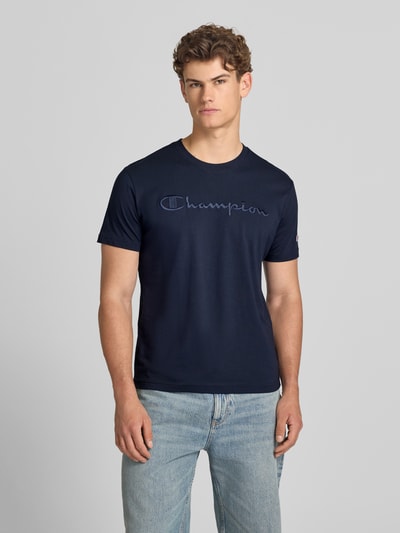 Männermodel trägt T-Shirt mit Label-Stitching mit Rundhalsausschnitt von CHAMPION in Dunkelblau aus Reine Baumwolle, Regular-Fit, Ganzkörperansicht von vorne. Rückenlänge bei Größe M: 68 cm.