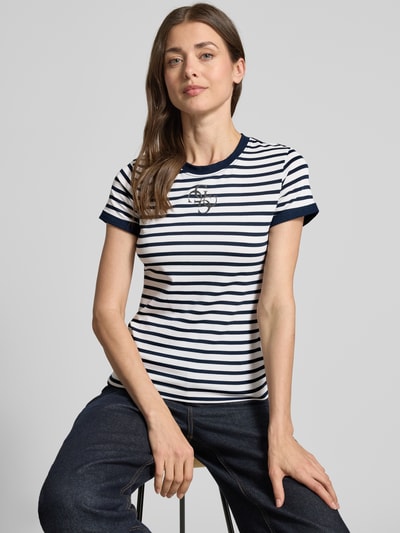Frauenmodel trägt T-Shirt mit Rundhalsausschnitt und Label-Print von Guess, Material-Mix mit Modal-Anteil, Körpernaher-Schnitt, Rückenlänge bei Größe S: 58 cm, gestreiftes Design in Weiß und Dunkelblau, Ganzkörperansicht von vorne.