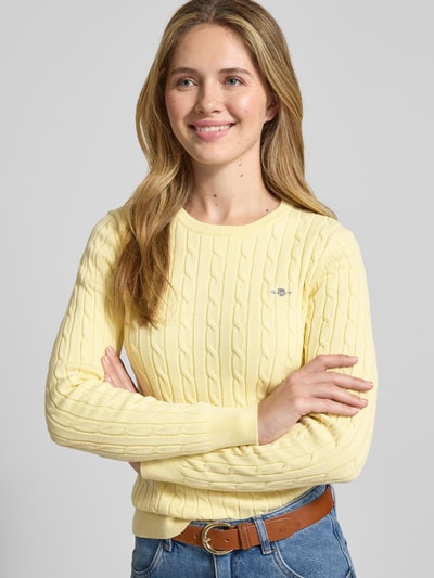 Frauenmodel trägt Strickpullover mit Zopfmuster und Label-Stitching von Gant in Gelb, Baumwoll-Mix mit Stretch-Anteil, Slim Fit, Rundhalsausschnitt, Nahaufnahme Oberkörper.