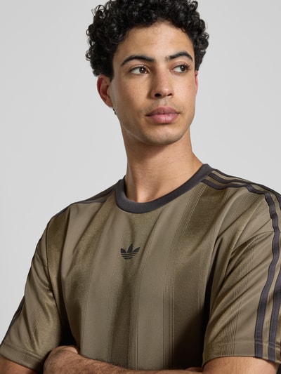 Männermodel trägt Regular Fit T-Shirt mit Logo-Print Modell 'JACQUARD' von adidas Originals in Braun, Nahaufnahme Oberkörper.