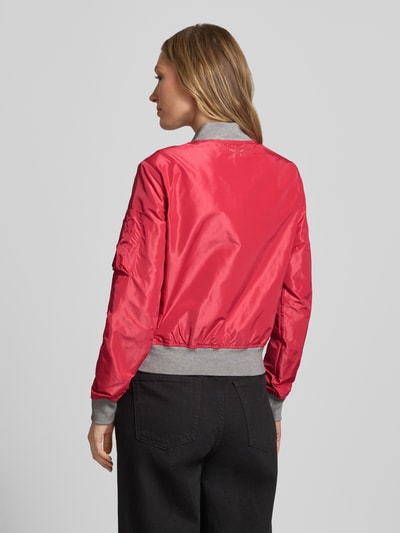 Frauenmodel trägt Bomberjacke mit Label-Patch und Reißverschlusstasche am Ärmel von Original Bombers in Rot mit grauen elastischen Abschlüssen, Lockere-Schnitt, Stehkragen, Rückenlänge 53 cm, Schulterbreite 37 cm, Brustweite 48 cm, Ärmellänge 63 cm, seitliche Eingrifftaschen mit Druckknopfverschluss, Material mit glatter Textur, Ganzkörperansicht Rückansicht.
