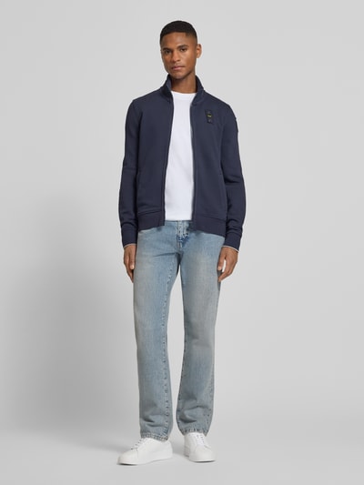 Männermodel trägt Sweatjacke mit Stehkragen Modell 'City New' von Blauer Usa aus Baumwoll-Mix, Slim-Fit, dunkelblau, Label-Detail, Ganzkörperansicht von vorne. Herren Sweatjacke, Reißverschluss, Rückenlänge 45 cm, Ärmellänge 84 cm, Größe M.