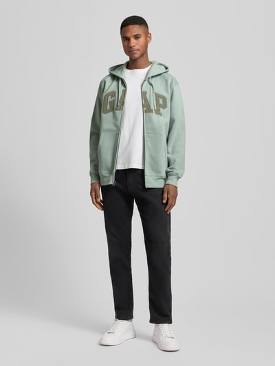 Männermodel trägt Sweatjacke mit Logo und Känguru-Tasche von GAP in Mintgrün, Baumwoll-Mix, Regular Fit, Ganzkörperansicht von vorne.
