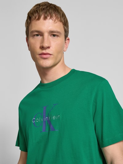 Männermodel trägt T-Shirt mit Label-Print und Rundhalsausschnitt von Calvin Klein Jeans in Grün, Reine Baumwolle, Regular-Fit, Nahaufnahme Oberkörper.