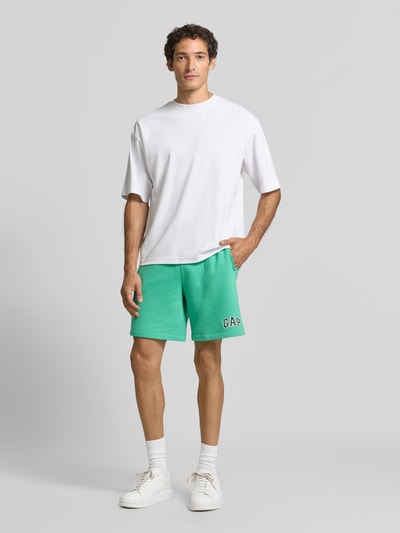Mannenmodel draagt Straight Fit korte broek met logostitching Model 'Heritage' van GAP, katoenmix, groen, binnenbeenlengte 20 cm, bandwijdte 40 cm, elastische band met tunnelkoord, ganzebodyvooraanzicht.