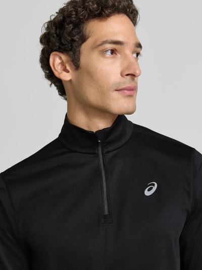 Männermodel trägt Funktionsshirt mit Logo und Reißverschluss von ASICS, schwarzer Material-Mix mit Stretch, Nahaufnahme Oberkörper