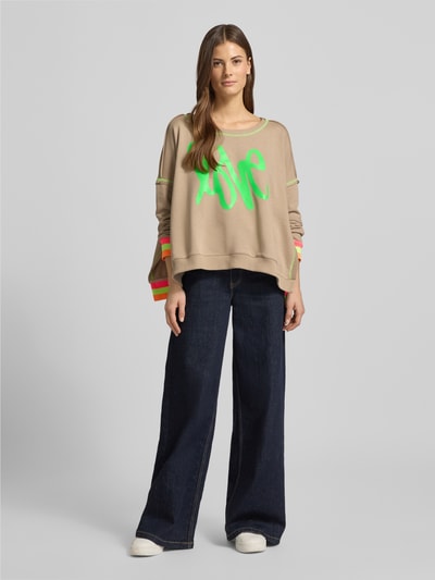 Vrouwenmodel draagt 'Oversized Sweatshirt mit gerippten Abschlüssen' van miss goodlife van pure katoen, oversized pasvorm, geribde boorden, ronde hals en statement print, kleuren beige en neon groen, volledige lichaamsaanzicht van voren.