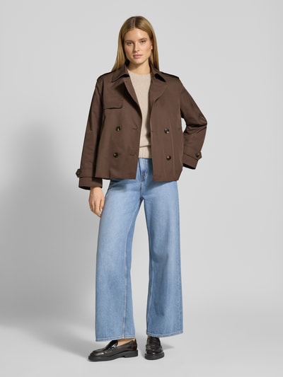 Modelka kobieca nosi Trenchcoat in kurzem Design mit Baumwoll-Anteil von Jake*s Casual, brązowy, prosta forma, z podwójnym zapięciem, szerokimi ramionami i krótkim krojem, materiałowy miks z bawełną, kieszenie boczne, pasek na ramionach i rękawach, szerokość w rozmiarze 36: 51 cm, szerokość ramion: 44 cm, długość rękawa: 60 cm, długość z tyłu: 64 cm, ujęcie całej sylwetki od przodu.