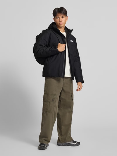 Männermodel trägt Jacke mit Logo und Ärmelriegeln von The North Face in Schwarz, regular Fit, Kapuze, Reißverschluss, Ganzkörperansicht von vorne.