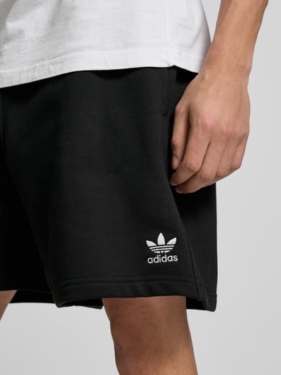 Männermodel trägt Regular Fit Sweatshorts aus Baumwoll-Mix Modell 'TREFOIL ESSENTIALS' von adidas Originals, Optik: Unifarben, Logo-Stitching, Bundabschluss: Elastisch, seitliche Eingrifftaschen, Materialverarbeitung: Sweat, Nahaufnahme Oberschenkel.