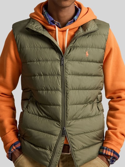 Männermodel trägt Regular Fit Weste mit Logo-Stitching von Polo Ralph Lauren in Olivgrün auf orangefarbenem Hoodie, Nahaufnahme Oberkörper. Herren Weste von Polo Ralph Lauren