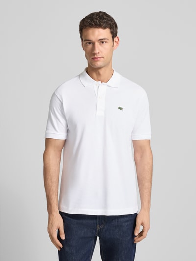 Männermodel trägt Poloshirt mit Label-Stitching Modell 'L.12.12 CORE' von LACOSTE in Weiß, aus reiner Baumwolle, Regular-Fit, Unifarbenes-Design, Polokragen, kurze Knopfleiste, gerippte Ärmelabschlüsse, Rückenlänge bei Größe M 72 cm, Ganzkörperansicht von vorne.