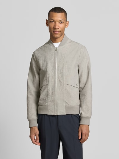 Männermodel trägt Bomberjacke mit Pattentaschen und Reißverschluss von PAUL SMITH in Grau, Struktur-Optik, Ganzkörperansicht von vorne, Loose-Fit, kurzer Stehkragen, gerippte Abschlüsse, Rückenlänge bei Größe M 65 cm, Schulterbreite 44 cm, Brustweite 53 cm, Ärmellänge 67 cm.