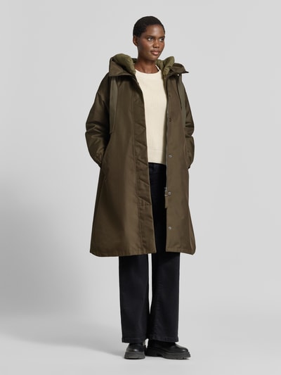 Frauenmodel trägt olivgrünen Parka mit Kapuze Modell 'AKIRA' von g-lab, gerader Schnitt, seitliche Eingrifftaschen, Ganzkörperansicht von vorne.