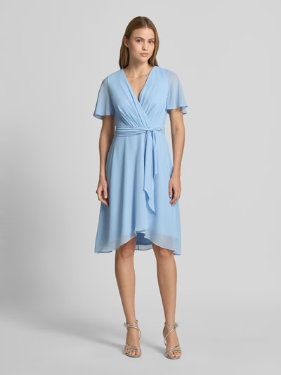 Vrouwenmodel draagt knielanges Cocktailkleid in Wickel-Optik van Christian Berg Cocktail in lichtblauw chiffon, a-lijn, v-hals, bindriem, voorkant volledige lichaamsweergave.