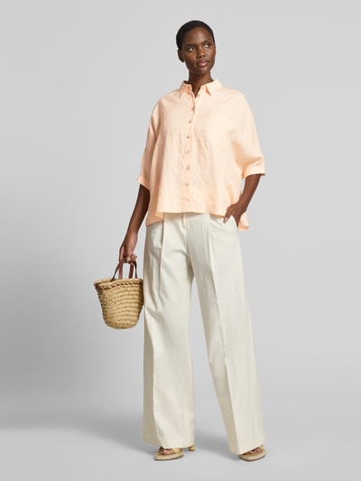 Frauenmodel trägt Relaxed Fit Leinenbluse mit Brusttasche von Emily Van den Bergh in zartem Beige, Hemdblusenkragen, 3/4-Arm, Ganzkörperansicht von vorne, Rückenlänge bei Größe S/M 63 cm, Ärmellänge 33 cm, reine Leinen-Textur.