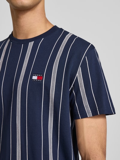 Männermodel trägt Regular Fit T-Shirt aus reiner Baumwolle von Tommy Jeans mit Optik: Allover-Muster und Label-Stitching, Nahaufnahme Oberkörper.