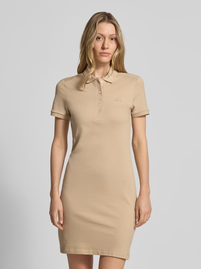 Frauenmodel trägt Slim Fit Polokleid aus Baumwoll-Mix von Lacoste in Beige, unifarben, Mini-Länge, Piqué-Textur, Ganzkörperansicht von vorne.
