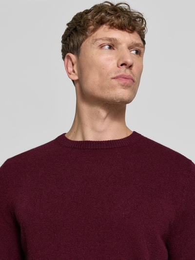 Männermodel trägt Kaschmirpullover mit gerippten Abschlüssen von Christian Berg Men in dunklem Burgunderrot, reines Kaschmir, Nahaufnahme Oberkörper.