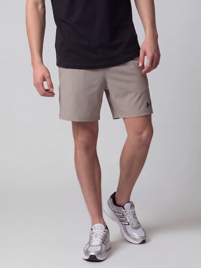 Männermodel trägt beige Regular Fit Sportshorts mit Logo-Print von Under Armour, glatte Textur, Ganzkörperansicht von vorne. Herren Sportshorts von Under Armour.