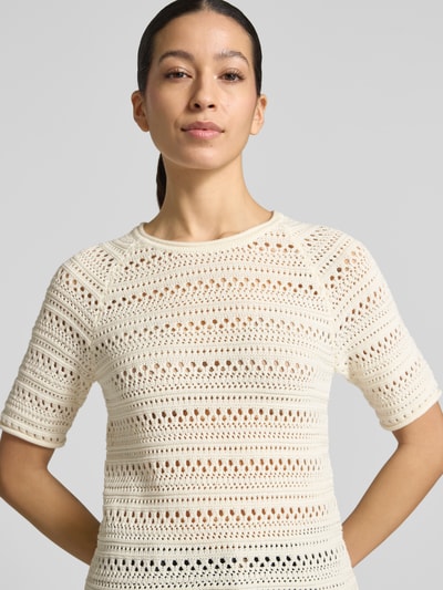 Modelka kobieca ma na sobie Strickshirt mit Rundhalsausschnitt od Jake*s Casual z bawełny, krój regular fit, zrolowany brzeg, długość tyłu 52 cm, długość rękawów 26 cm, kremowa tekstura ażurowa, zbliżenie na górną część ciała.