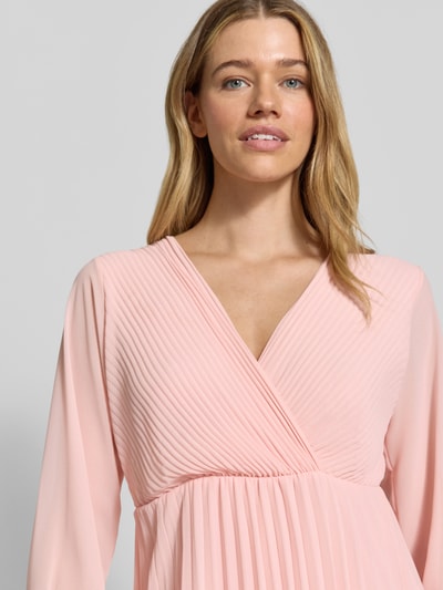 Frauenmodel trägt knielanges Kleid mit Plisseefalten Modell 'Im44sa' von ZABAIONE in Wickel-Optik, taillierter Schnitt, Nahaufnahme Oberkörper. Rückenlänge bei Größe S 90 cm, Brustweite 38 cm, Ärmellänge 52 cm. Zart rosafarbene Textur, feine Faltenstruktur.
