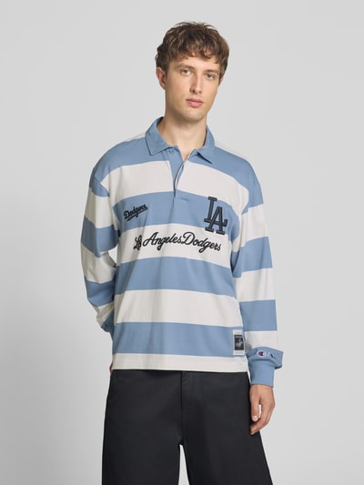 Männermodel trägt Relaxed Fit Poloshirt aus reiner Baumwolle von Champion, breite blaue und weiße Streifen, Langarm, Statement-Stitching, Ganzkörperansicht von vorne.