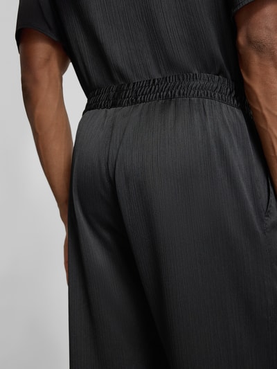 Mężczyznamodel nosi Hose mit elastischem Bund Modell 'Houston' von Les Deux, plisowany, krój loose fit, szerokość w rozmiarze M: 42 cm, długość nogawki od wewnątrz: 81 cm, ciemnoszary materiał z subtelną fakturą, zbliżenie tylnej części spodni, detal.