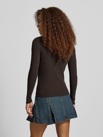 Frauenmodel trägt Slim Fit Langarmshirt aus Baumwoll-Mix Modell 'SARA SHARAI' von ONLY in Dunkelbraun, kombiniert mit blauem Jeansrock, Ganzkörperansicht Rückansicht. Damen Langarmshirt von ONLY.