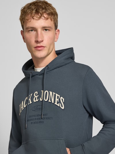 Männermodel trägt Regular Fit Hoodie aus Baumwoll-Mix Modell 'Denver' von JACK & JONES in Dunkelblau mit Kapuze und Känguru-Tasche, Nahaufnahme Oberkörper. Rückenlänge und Ärmellänge bei Größe M je 67 cm, elastische Abschlüsse.