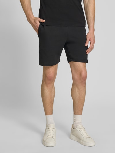 Männermodel trägt Regular Fit Sweatshorts aus reiner Baumwolle von Lacoste in Schwarz, unifarben, 5-Pocket-Design, Nahaufnahme Oberkörper bis Knie.
