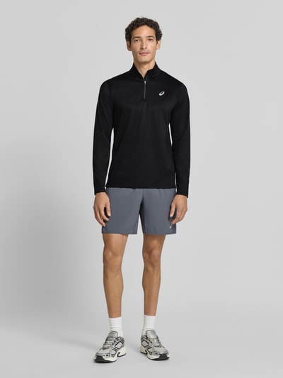 Männermodel trägt Funktionsshirt mit Logo und Reißverschluss von ASICS, schwarz, Regular Fit, Material-Mix, Longsleeve, Ganzkörperansicht von vorne.
