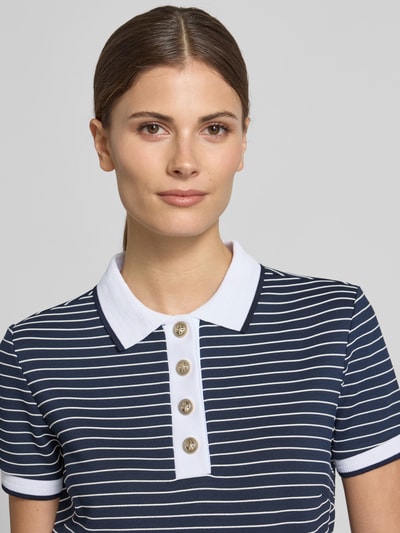 Modelka kobieca nosi koszulkę polo Cropped Poloshirt aus Viskose-Mix Modell 'ALPHONSINE' od Guess, mieszanka wiskozy z dodatkiem streczu, wzór w paski, listwa guzikowa, długość tyłu w rozmiarze S: 49 cm, zbliżenie na górną część ciała.