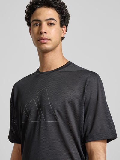 Mężczyznamodel nosi Regular Fit T-Shirt in Mesh-Optik mit Logo-Print od adidas Training, czarny, okrągły dekolt, krój regular fit, nadruk logo, długość tyłu w rozmiarze M: 75 cm, siateczkowa faktura, zbliżenie na górną część ciała.