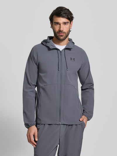 Männermodel trägt Regular Fit Jacke mit Logo-Print Modell 'Vibe' van Under Armour, elastisch materiaal, capuchon, grijs, voorkant, halftotaal.