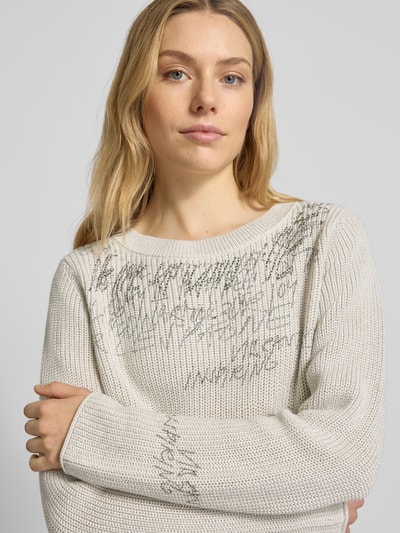 Kobiece model prezentuje Sweter z dzianiny z obszyciem ozdobnymi kamieniami od monari, mieszanka bawełny, krój regular fit, okrągły dekolt, długość tyłu 60 cm, długość rękawów 64 cm, jasny kolor, faktura dzianiny, widoczne zdobienia, ujęcie: zbliżenie na górną część ciała z przodu.