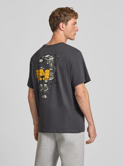 Männermodel trägt T-Shirt aus reiner Baumwolle Modell 'Gear Up Get Out' von The North Face in Dunkelgrau mit Logo-Print, Ganzkörperansicht Rückansicht.