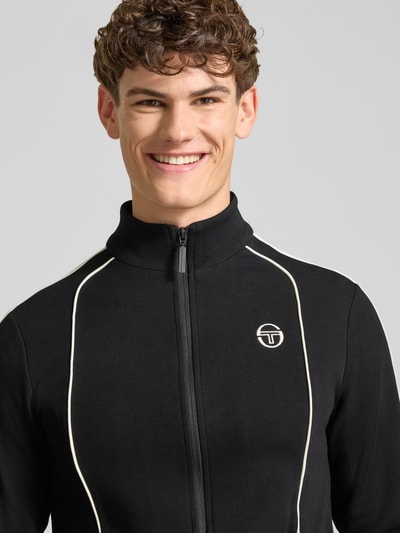 Männermodel trägt Slim Fit Tracksuit mit Logo-Stitching Modell 'Egeo' von SERGIO TACCHINI, Schwarztöne, Nahaufnahme Oberkörper.