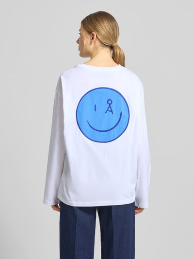Kobiece modelka nosi Oversized Langarmshirt aus reiner Baumwolle Modell 'FIETAA SMILE' von Armedangels, biały kolor, duży niebieski nadruk logo smile na plecach, unifarbny, długi rękaw, krój oversize, materiał bawełna, widok całej sylwetki od tyłu.