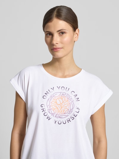 Frauenmodel trägt T-Shirt mit Statement-Print von G.I.G.A. DX in Weiß mit Rundhalsausschnitt, Material-Mix, Nahaufnahme Oberkörper.