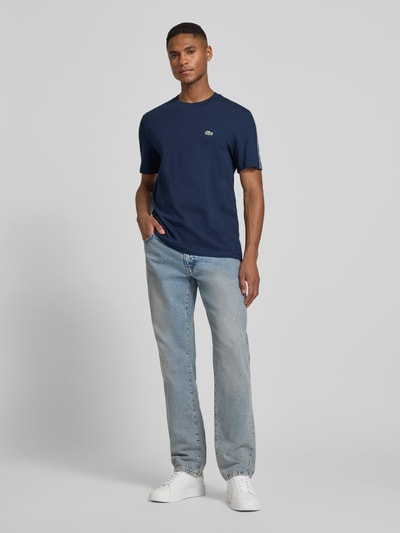 Męski model nosi Regular Fit T-Shirt aus reiner Baumwolle od Lacoste, gładka niebieska bawełna, label-tape, krój regular fit, krótki rękaw, dekolt okrągły, widok całej sylwetki z przodu.