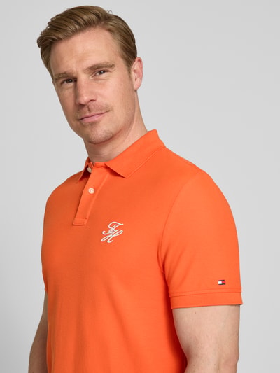 Męski model nosi Regular Fit Poloshirt aus reiner Baumwolle od Tommy Hilfiger, pomarańczowy, gładki pikowany materiał, logo, krótki rękaw, detal na piersi, krój regular fit, widok na górną część ciała z przodu.