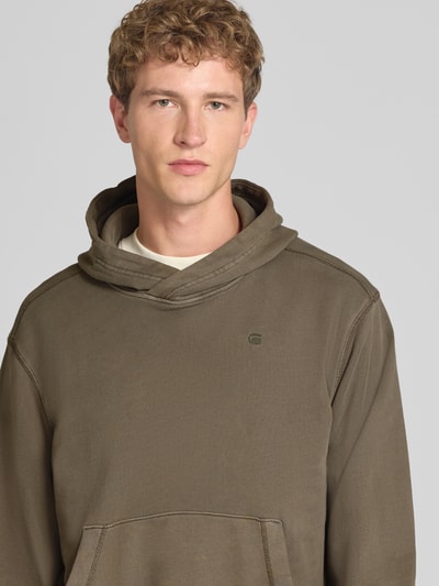 Männermodel trägt Regular Fit Hoodie aus reiner Baumwolle von G-Star RAW in Olivgrün, glatte Struktur, Nahaufnahme Oberkörper.