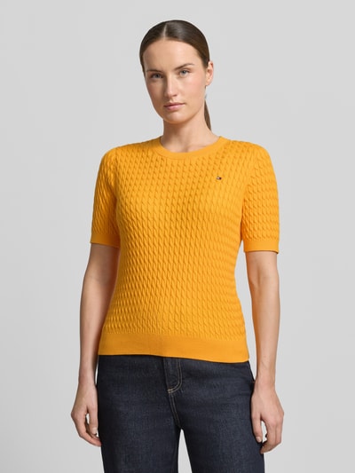 Frauenmodel trägt Slim Fit T-Shirt aus reiner Baumwolle von Tommy Hilfiger, Optik: Unifarben, Zopfmuster, Logo-Detail, Strick, Rundhals, Kurzarm, Ärmelabschluss und Rumpfabschluss gerippt, Farbe Gelb, ganzkörperansicht von vorne.