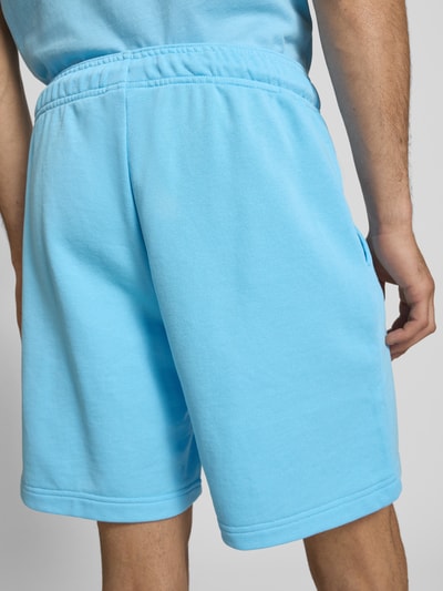 Männermodel trägt Sweatshorts mit Logo und elastischem Bund von CHAMPION in Hellblau, Baumwoll-Mix, Regular Fit, Ganzkörperansicht Rückansicht.