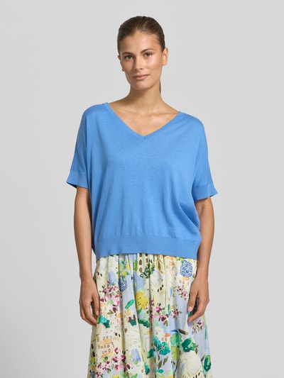 Frauenmodel trägt Strickshirt aus Viskose-Mix mit V-Ausschnitt von Milano Italy in Himmelblau, Regular Fit, Halbarm, glatte Textur, kombiniert mit floralem Rock, Nahaufnahme Oberkörper.