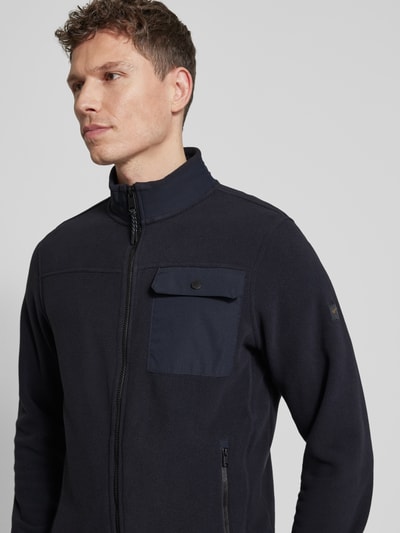 Męski model nosi Bluza rozpinana mit Stehkragen und Brusttasche von camel active, krój regular fit, kolor ciemnogranatowy, zamek błyskawiczny, Brustasza oraz wpuszczane kieszenie zapinane na zamek błyskawiczny, długość tyłu w rozmiarze M: 68 cm, długość rękawów: 67 cm, nahaufnahme górna część ciała.